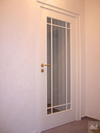 Weiße Innentür mit Glaseinsatz und goldfarbenem Türgriff in modernem Flur.