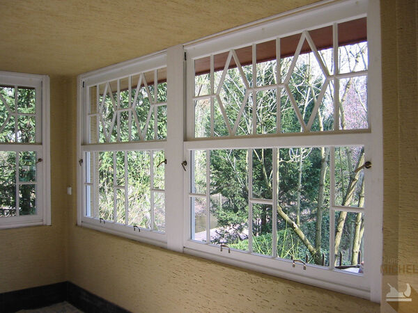Große weiße Holzfenster mit Sprossen und Blick auf einen grünen Garten im Wintergarten.