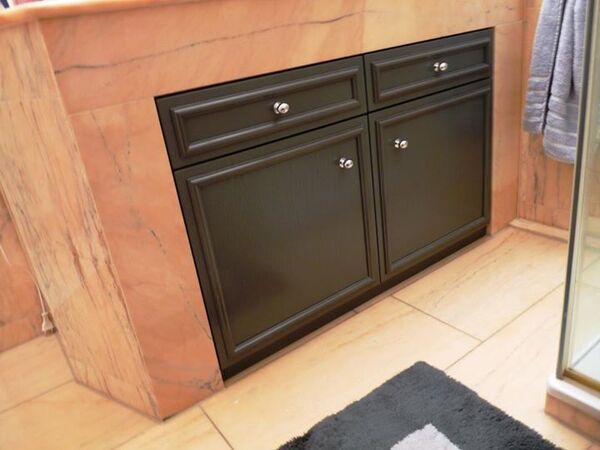 Schwarzer Badezimmerunterschrank mit zwei Türen und Schubladen auf beigem Marmorboden.