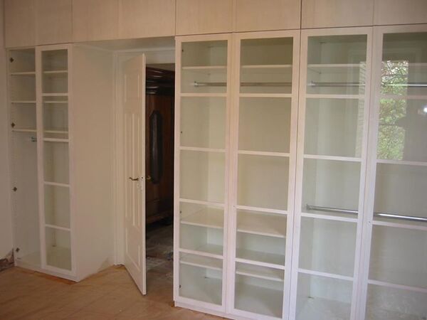 Großer, moderner Einbauschrank mit Glastüren und Regalböden in einem hellen Raum.