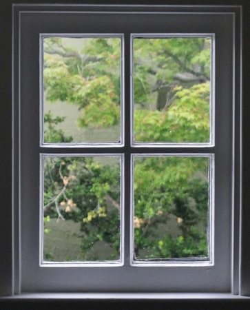 Blick durch ein Fenster mit sechs Scheiben auf grüne Bäume und Natur im Hintergrund.