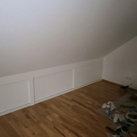 Weiß gestrichene Verkleidung unter Dachschräge mit Parkettboden im renovierten Dachzimmer.