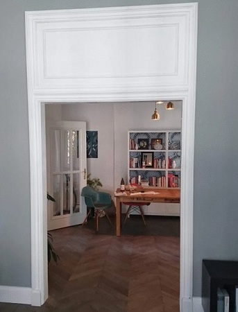 Blick durch eine weiße Tür in ein modernes Arbeitszimmer mit Bücherregal und Schreibtisch.