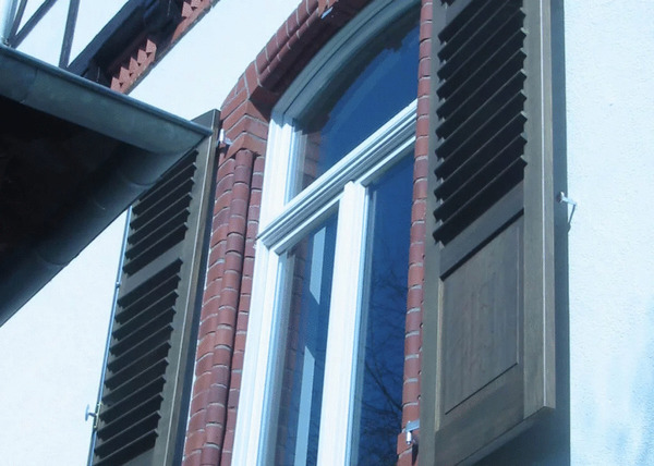 Historisches Hausfenster mit weißen Sprossen, Backsteinrahmen und braunen Fensterläden.