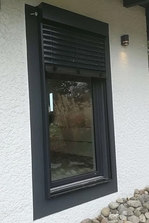 Modernes Fenster mit schwarzem Rahmen und Außenjalousie an weißer Putzfassade.