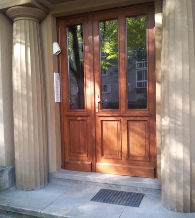 Holztür mit Glaseinsätzen und Marmorstufen, flankiert von zwei Säulen am Hauseingang.