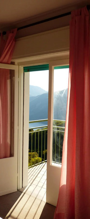Sonniger Ausblick vom Balkon mit rosa Vorhängen und Bergpanorama im Hintergrund.