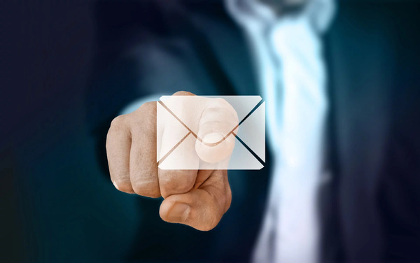 Eine Hand tippt auf ein digitales E-Mail-Symbol vor unscharfem Hintergrund.