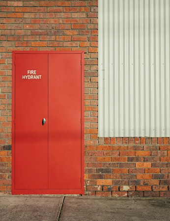 Roter Hydrantenschrank mit Aufschrift an Backsteinwand neben weißem Blech, Brandschutz Symbol.