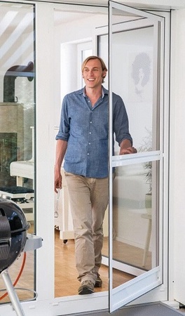 Mann öffnet Fliegengittertür auf Terrasse, Insektenschutz für Zuhause, modernes Design.