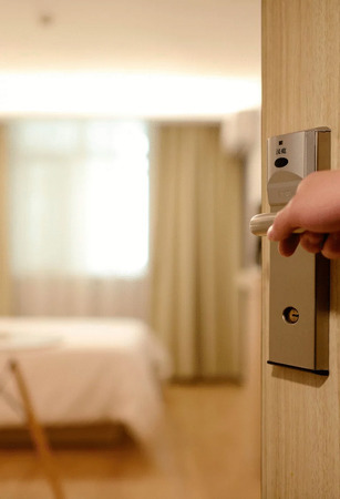 Eine Hand öffnet eine Hotelzimmertür mit moderner Schließkarte, dahinter ein Bett.