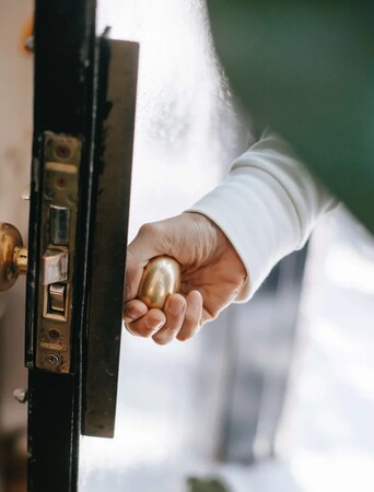 Hand öffnet Haustür mit goldenem Türgriff, Fokus auf Sicherheit und Eingang.